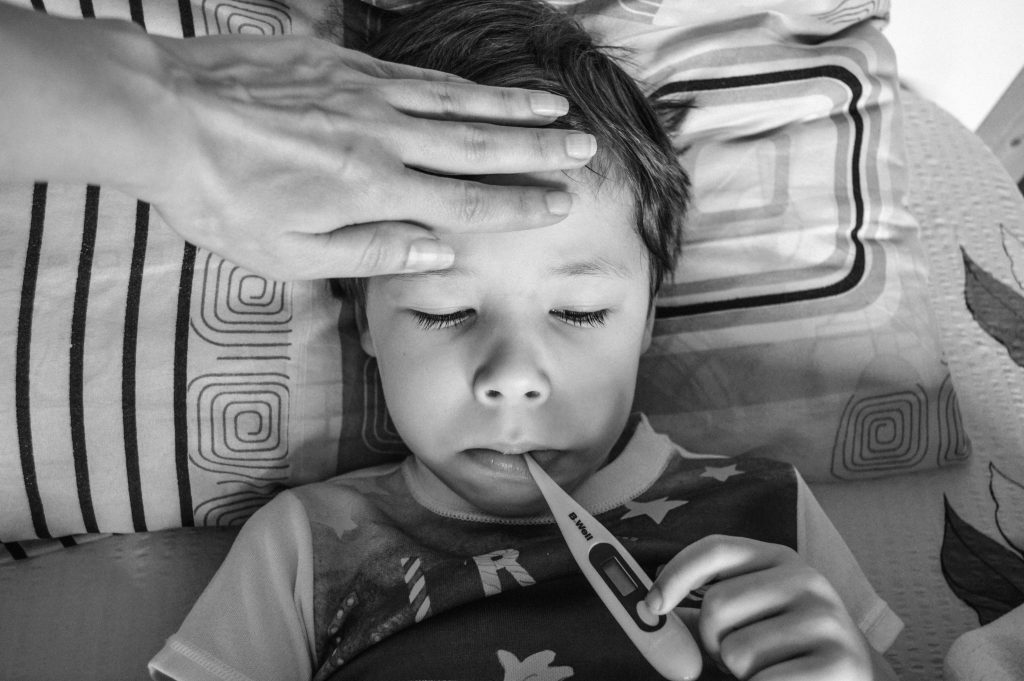 A child resting with a thermometer, monitored by caring hand, indoors.
